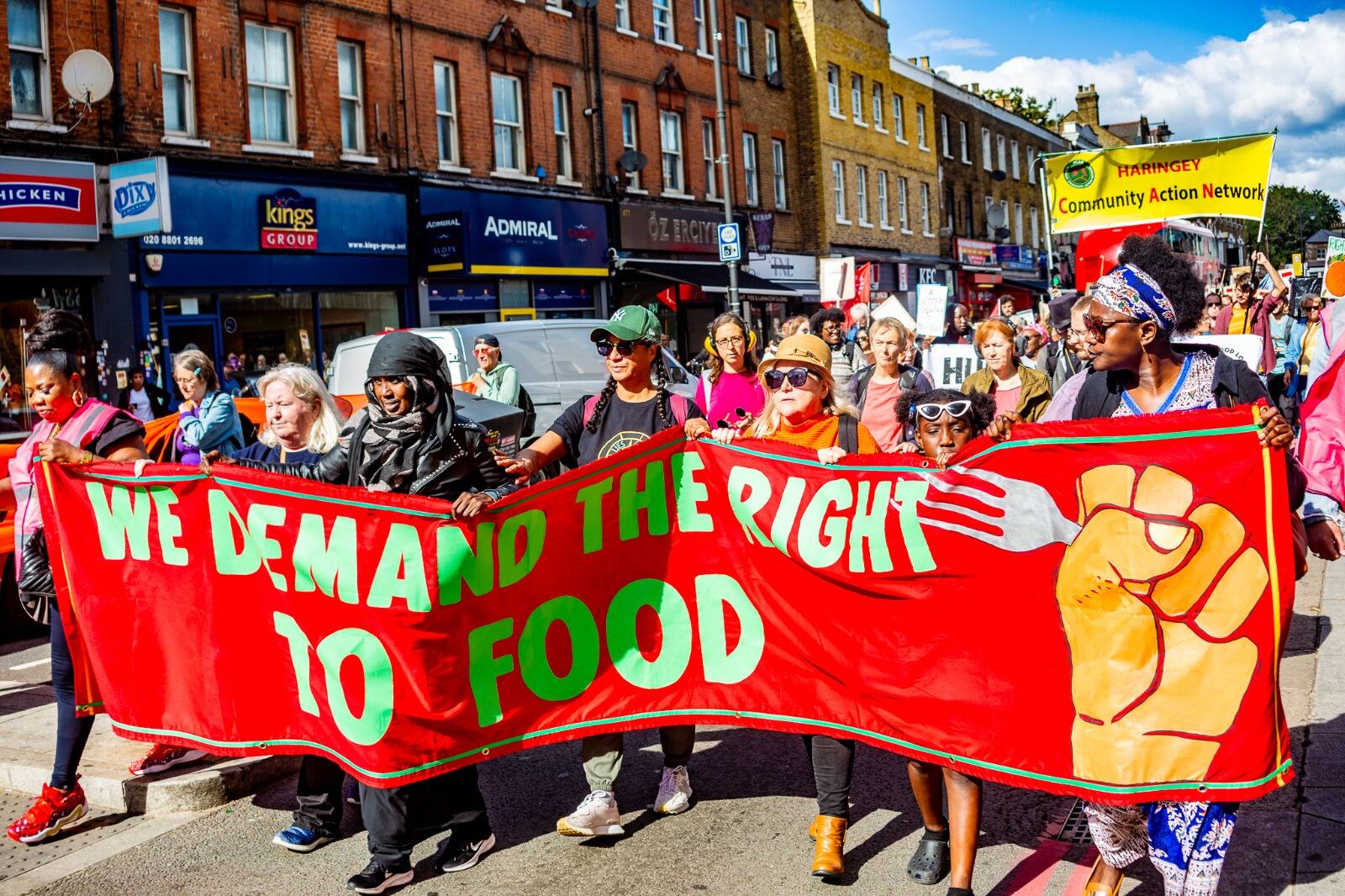 Marchers fill a Haringey street behind a red "We demand the right to food" banner, with the yellow Haringey Community Action Network banner flying behind.
